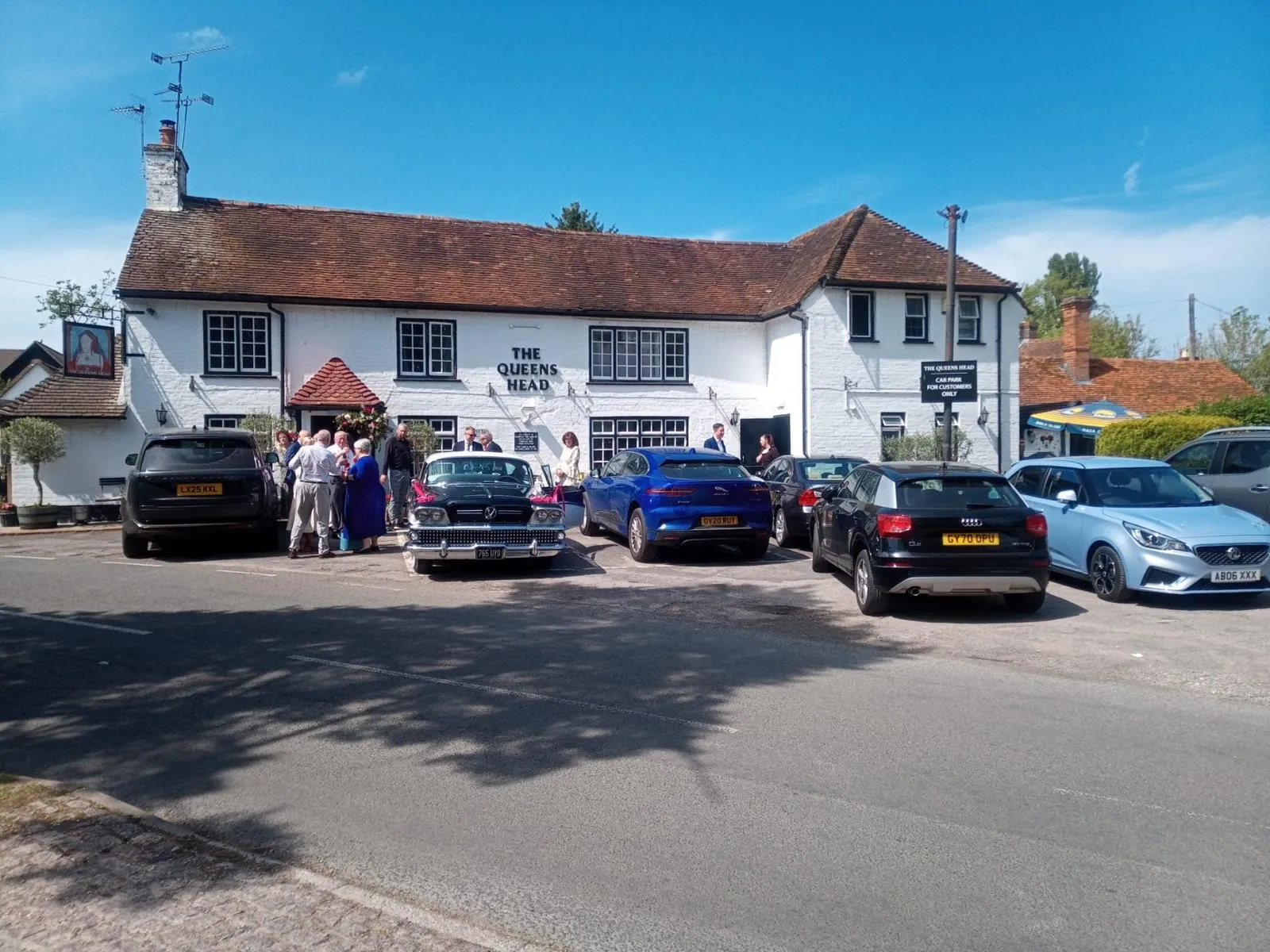 Wedding guests gathered outside the pub on a sunny afternoon, with a vintage wedding car in the car park